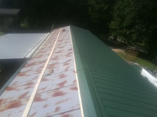 Old rusted panels beside newly installed green metal roofing — Wind Damage Roof Repair by Roofing Brothers in Judsonia