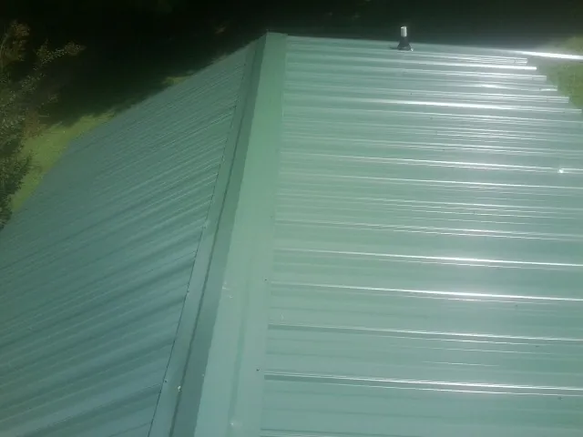 New green metal panels meeting at the ridge of a roof — Flat Roof Repair work by our crew in Judsonia