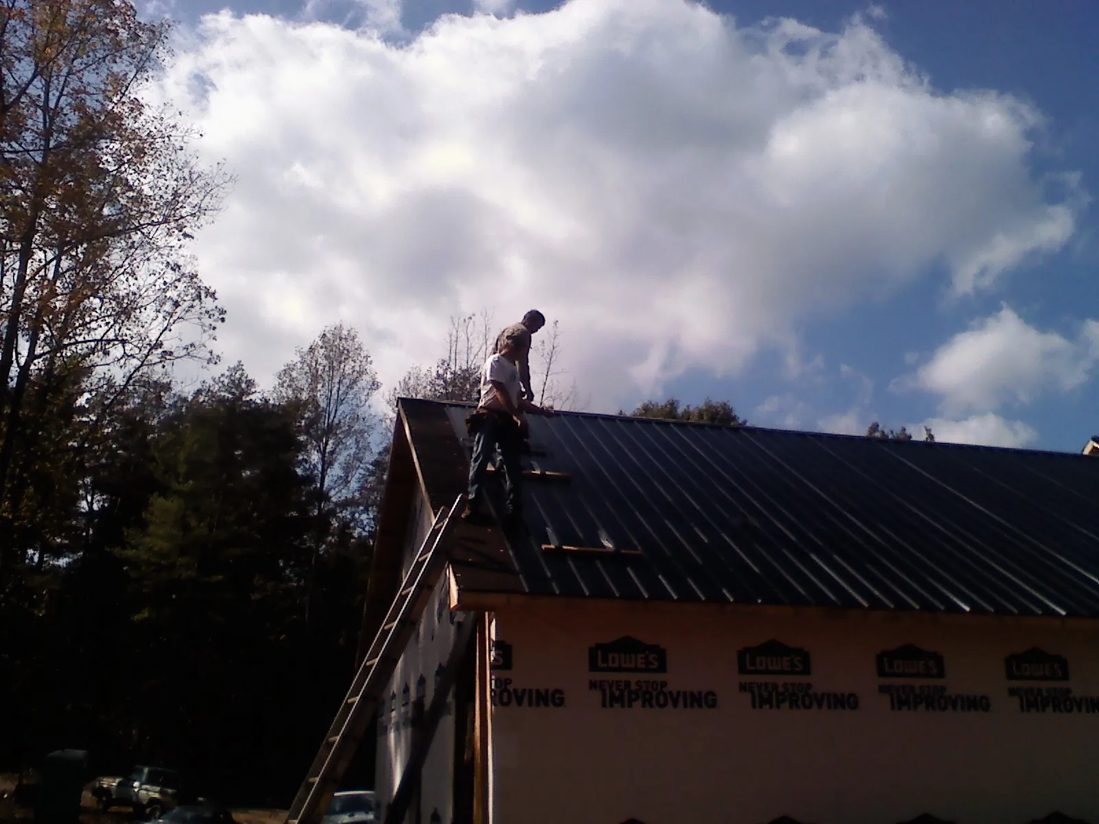 Roofer fastening dark metal panels high against a cloudy sky, from a Roof Inspection job in Judsonia