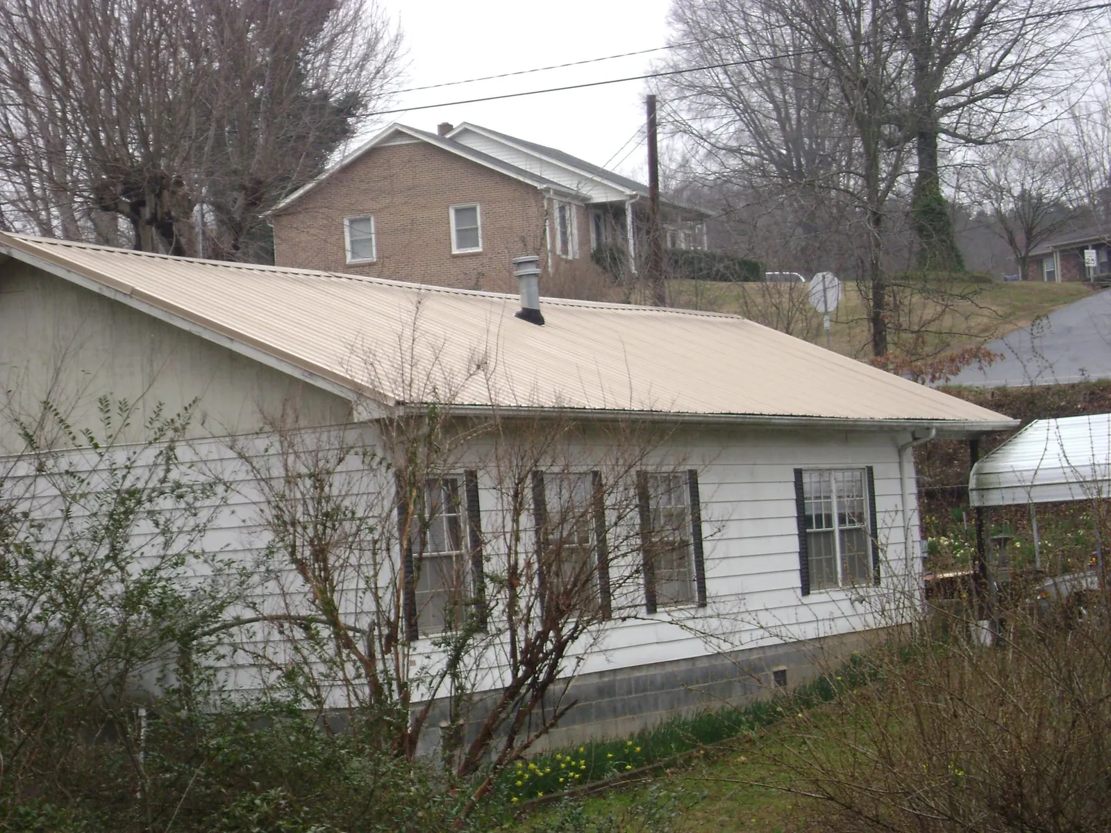 Tan metal roof on a white sided house set into a hillside — Commercial Roofing by Roofing Brothers in Judsonia